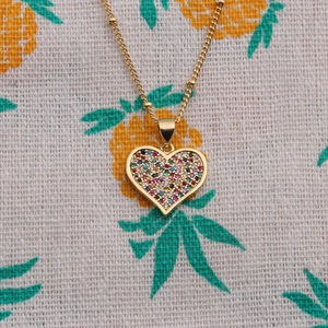 Collier cœur doré avec zircons colorés et chaîne perlée sur fond à motif ananas