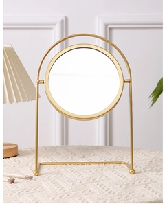Close-up of golden desktop makeup mirror with round metal frame and stable U-shaped stand