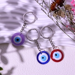 Three-piece evil eye keychain set in purple, blue and red on white textured background