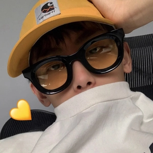 Close-up of retro thick black frame sunglasses with yellow lenses worn with a yellow cap