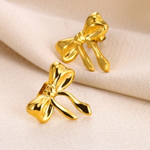 Detailed macro view of 18K gold polished bow earrings on a soft beige fabric background