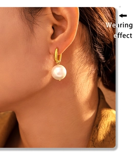 Close-up of gold U-shaped hoop earrings with white pearl pendants on a model