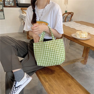 Lifestyle shot of green checkered canvas tote bag held by a model on a wooden bench