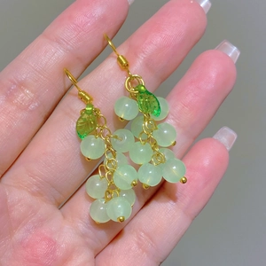 Close-up of vintage grape-shaped drop earrings with green beads and gold leaf charms