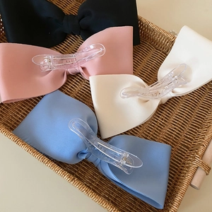 Detailed view of large fabric bow hair clips in four colors inside a vintage rattan basket