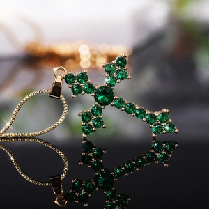 Macro view of gold cross pendant with emerald green cubic zirconia and box chain