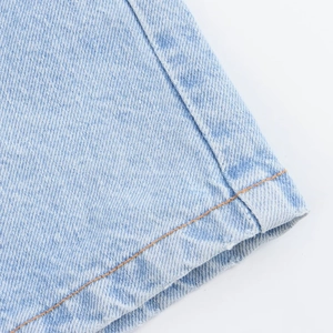 Detailed close-up of light blue denim fabric texture with orange contrast stitching