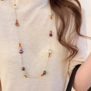 Détail de perles en résine colorées et chaîne dorée sur fond de pull en maille beige