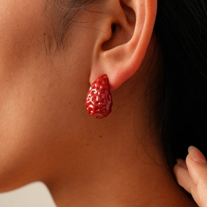 Detailed close-up of a glossy red strawberry-shaped earring worn on a model ear
