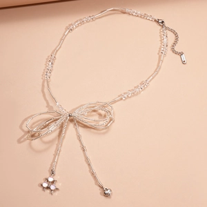 Detail of silver bow necklace with glass beads and a heart pendant on beige background