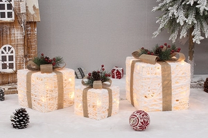 Close-up of three white rattan lighted Christmas gift boxes with pine cones and brown bows