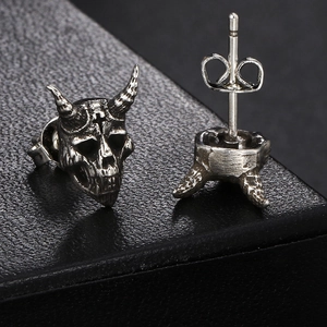 Macro detail of gothic skull earrings with devil horns and cross in vintage silver