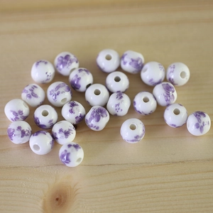 Macro detail of white ceramic beads with purple floral patterns on a wooden surface