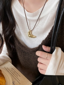 Close-up of golden croissant pendant on a black cord necklace worn for autumn fashion