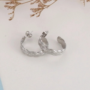 Detailed view of silver braided texture earrings on minimalist beige background with dried floral