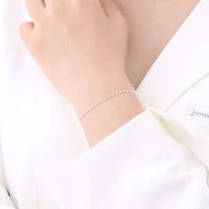 Close-up of minimalist pink beaded bracelet worn on wrist with elegant white suit
