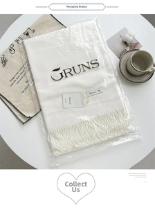 Close-up of a white cashmere-feel scarf with tassels and brand tag in premium packaging