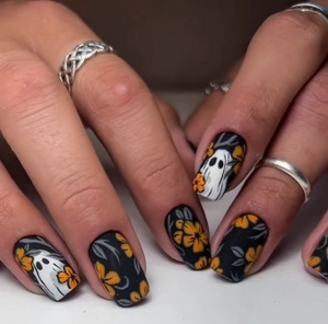 Detail of matte black Halloween nails featuring cute white ghosts and orange floral accents