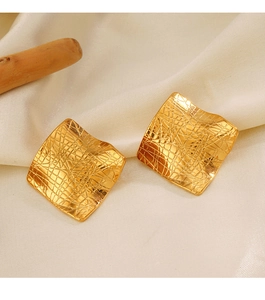 Macro detail of gold irregular square earrings with textured mesh on beige satin fabric