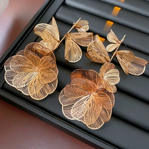 Macro shot of large golden hollow wire flower earrings on a black striped jewelry tray