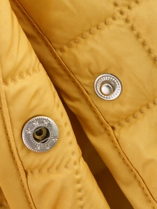 Détail du tissu matelassé jaune et bouton-pression en métal argenté avec relief