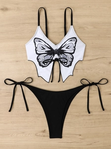 Detail of white bikini top with butterfly print and side-tie black bottoms on wood