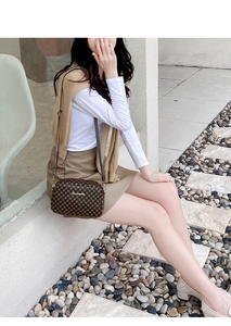 Detail of checkered crossbody camera bag with metal chain strap worn on outdoor stairs