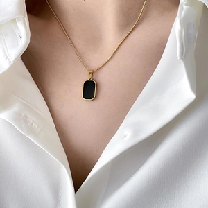 Detail of a minimalist gold box chain necklace with a black rectangular onyx pendant