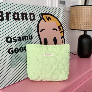 Detail of light green quilted cosmetic bag with 3D flower texture and logo patch