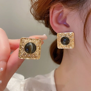 Macro detail of vintage square earrings with black gemstone and engraved gold-tone metal