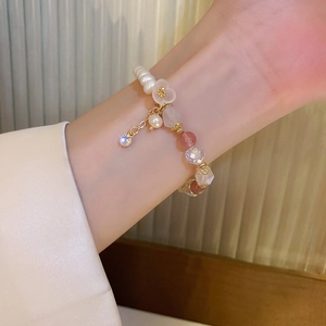 Detail of pink strawberry quartz and pearl bracelet with golden flower charm on wrist