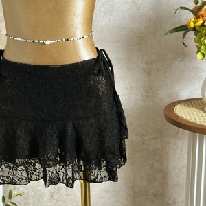 Detail of black mesh lace mini skirt with ruffled hem and decorative side tie closure