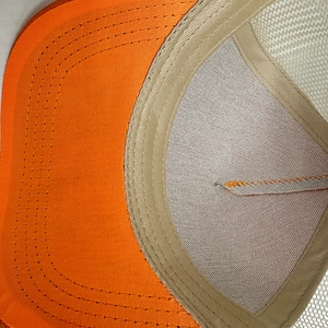 Detail von atmungsaktivem Mesh und Doppelnaht an einer orange-beigen Trucker-Mütze