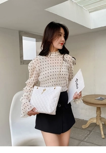 Detail of white quilted tote bag with gold chain strap and pearl charm on a model