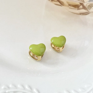 Close-up of green heart enamel earrings with gold edges on a ceramic plate
