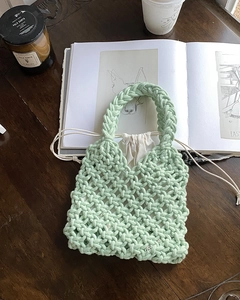 Detail of light green hand-woven bag with cream inner pouch on a dark wooden table
