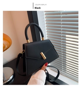 Detail of a black leather square handbag with golden metal accents and adjustable strap