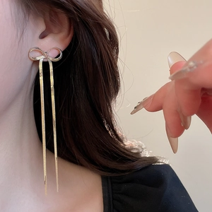 Close-up of golden bow long tassel earrings worn by a model in a warm minimalist setting