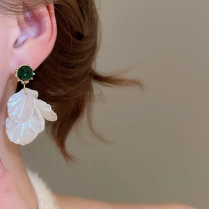 Detail of floral drop earrings with green gemstone and white shell petals on a model