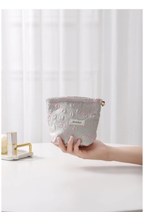 Close-up of a floral relief makeup bag in grey and pink held by hand for scale