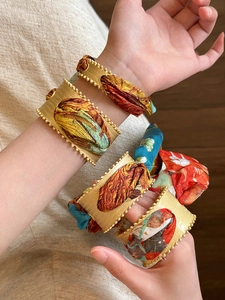 Detailed view of layered matte gold open bangles with colorful silk fabric textures