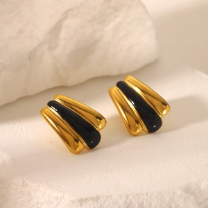 Macro shot of gold-plated fan-shaped earrings with black enamel on a stone surface