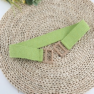 Detail of green elastic woven belt with textured gold metal buckle on a woven mat
