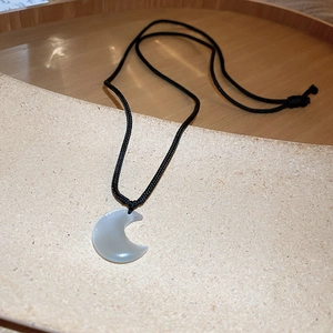 Detail of a crescent moon resin pendant with adjustable black braided cord necklace