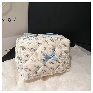 Close-up of beige floral quilted cosmetic bag with blue zipper and bow detail