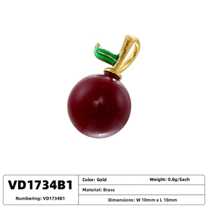Macro detail of red enamel cherry pendant with gold brass stem and green leaf charm