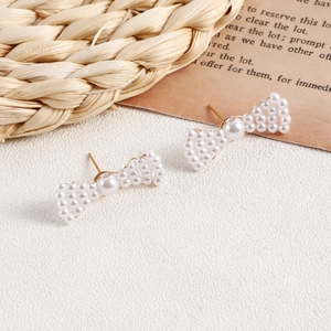 Close-up of handmade woven pearl bow earrings with gold accents and intricate textures