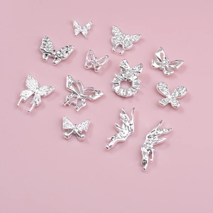Macro detail of 12 silver hollow butterfly nail charms with rhinestones on pink background