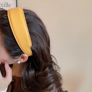 Detail of ginger yellow pleated faux leather headband showing texture and thickness on hair