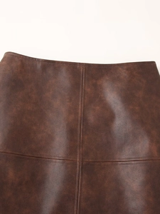 Détail de la texture en similicuir marron et des coutures sur la jupe courte